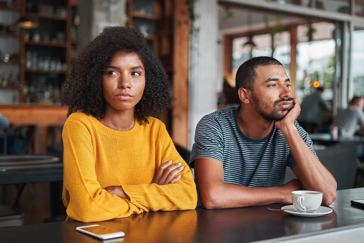 young black couple sitting next to each other at a coffee shop and not speaking or making eye contact