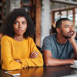 young black couple sitting next to each other at a coffee shop and not speaking or making eye contact