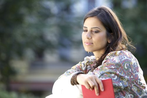 middle eastern woman looking pensive while holding a journal