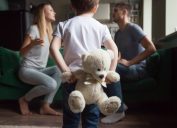 kid holding a teddy bear in front of two parents who are arguing