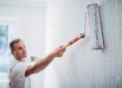 man painting walls in his home with a paint roller