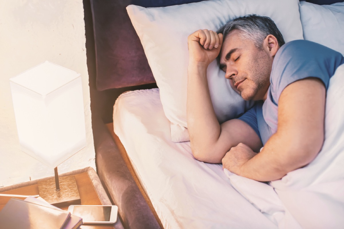 middle aged white man sleeping in blue t-shirt next to lamp