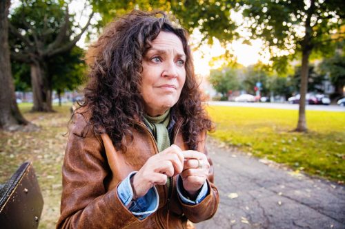 Anxious middle aged woman in crisis outdoors in park on an outdoors afternoon