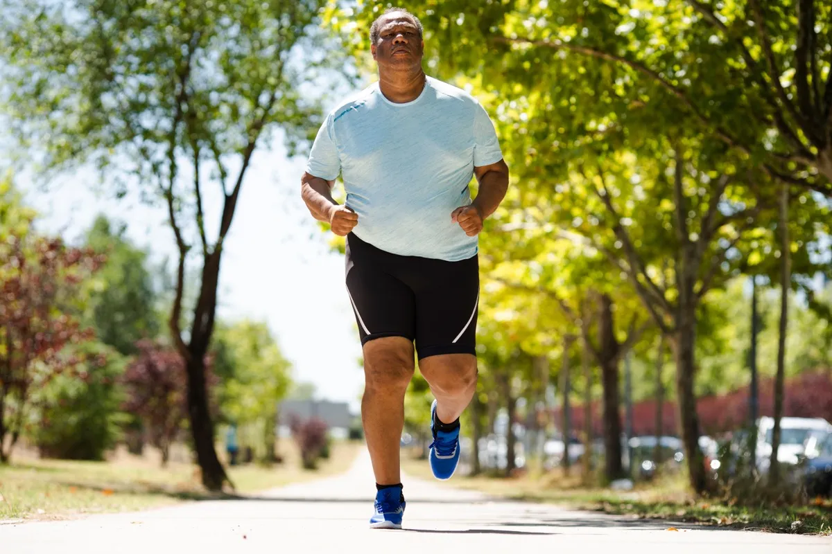 Overweight black man running outside getting some exercise in