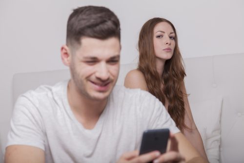 woman looks very suspicious of her husband smiling when receiving a text. Is he cheating?