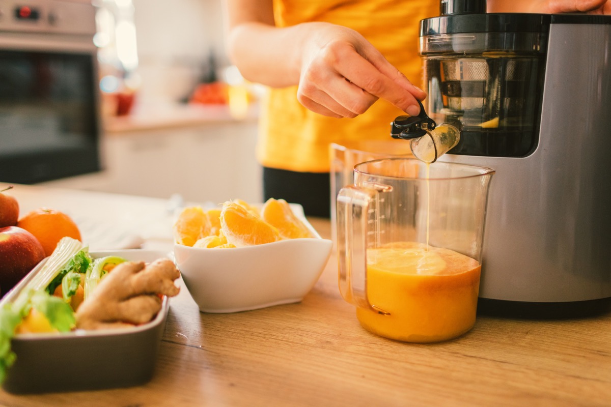 Mid adult woman making cold-pressed juice in the kitchen. Focus on cold-pressed juicer