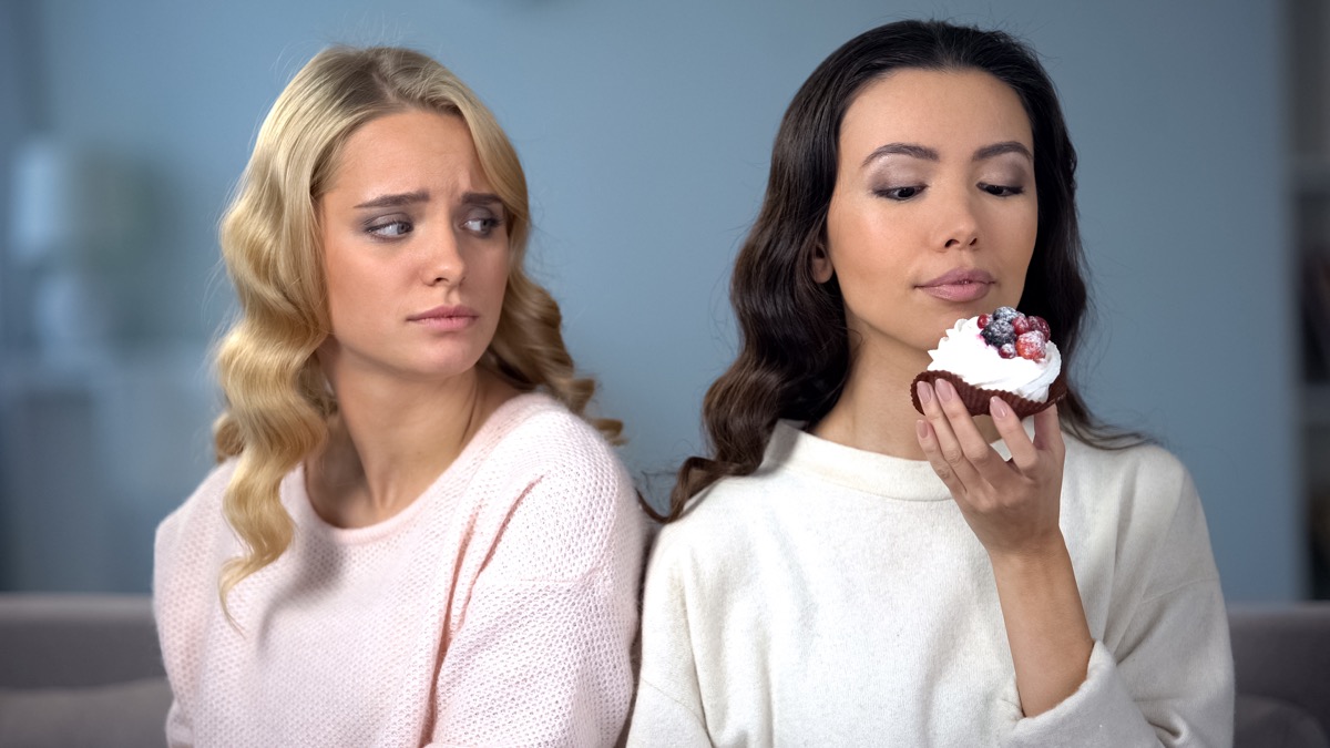Woman jealous of her skinny friend eating a cupcake