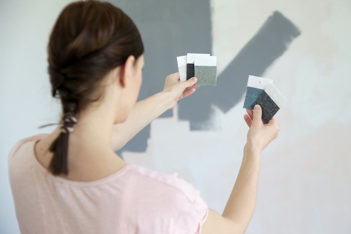 young woman choosing between paint swatches of gray for her wall