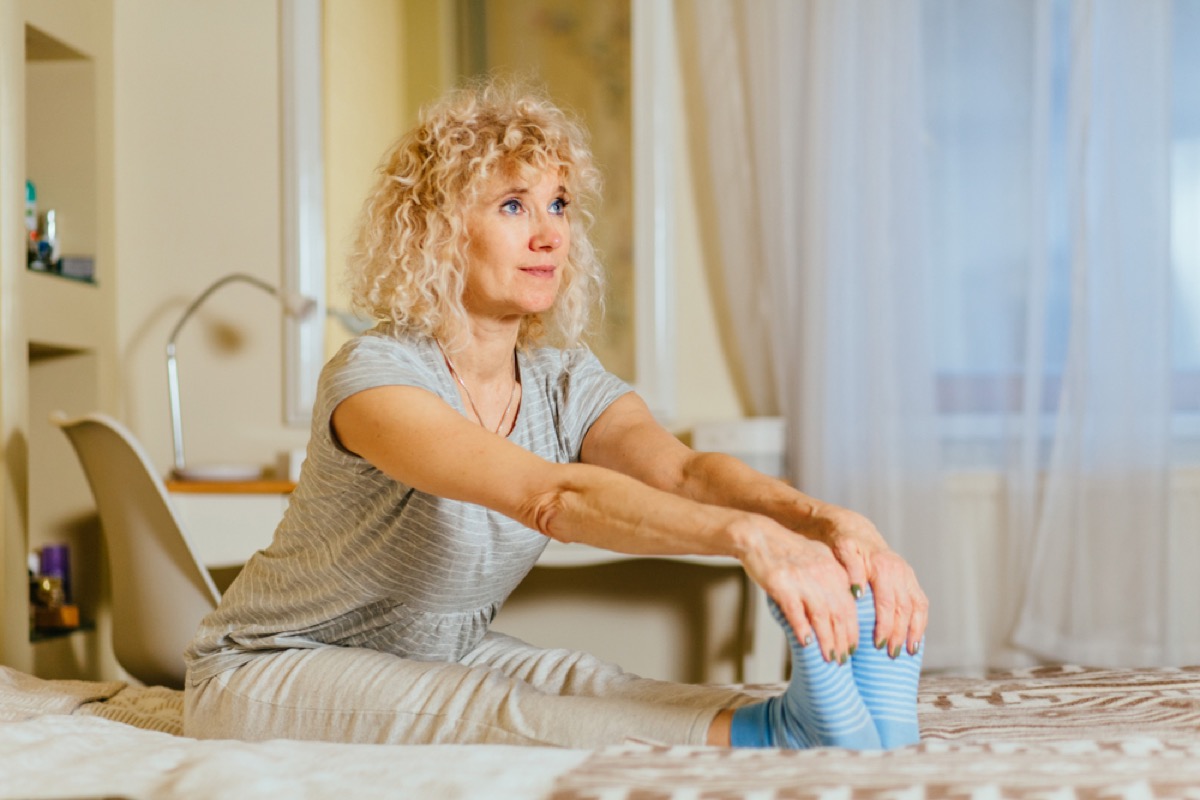 middle age white woman stretches on bed by holding onto her feet