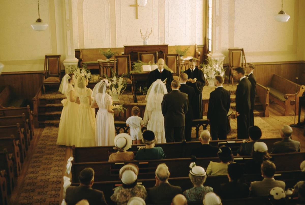 Wedding at a missionary church, bridal party, bride and groom standing in the front of the church with the pastor, high-angle view, attendees sitting in pews and wearing formal outfits in 1940s