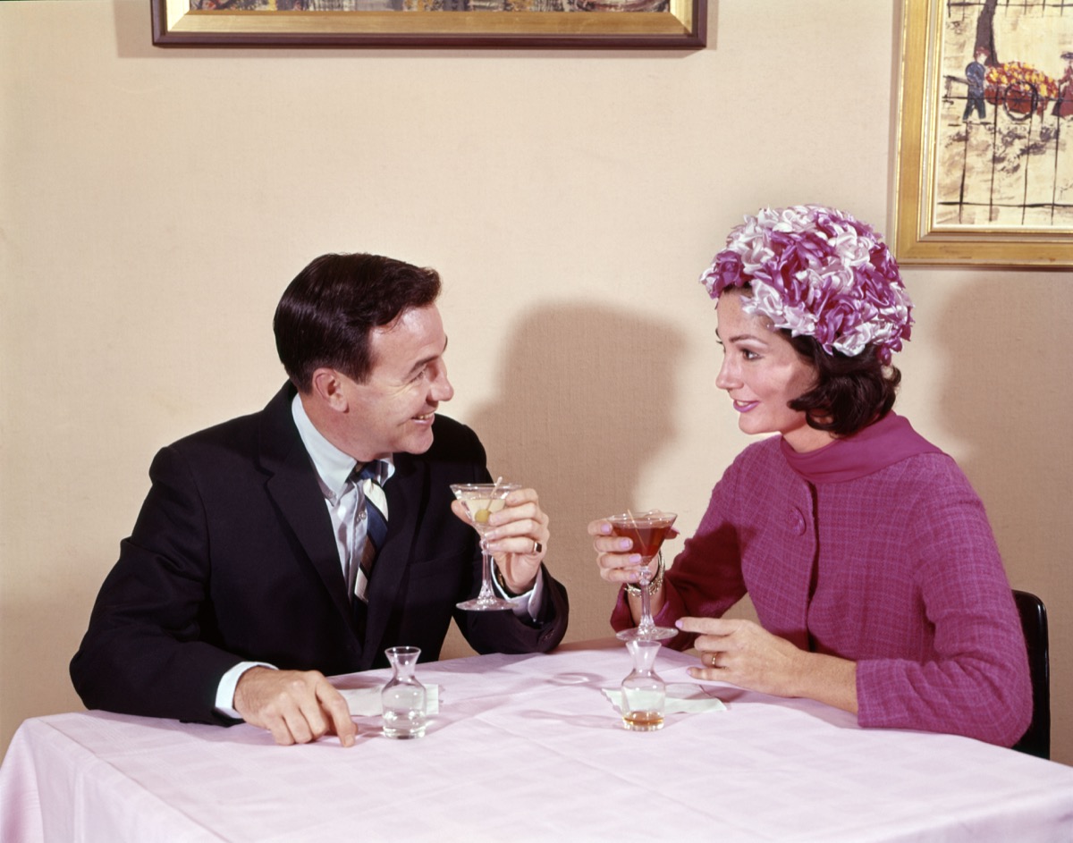 1960s couple enjoys cocktails, she wears floral hat