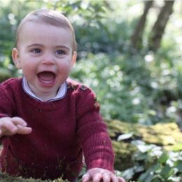 Prince Louis in maroon sweater sits in wooded area, official photo by Kate Middleton