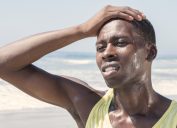 close up of black man sweating outside with his hand on his forehead