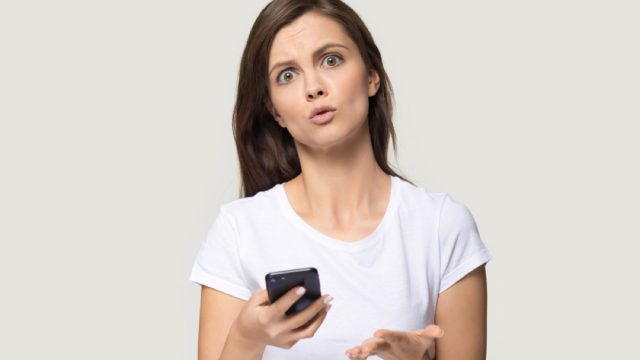 white woman holding phone and looking confused