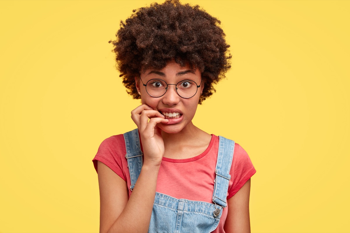 african american girl with glasses and overalls nervously bites nails, bad childhood habit