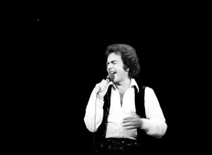Neil Diamond performs in white wide collar shirt and black vest
