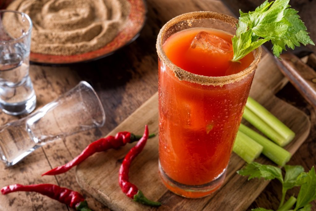 Bloody Mary Caesar Cocktail on wooden table with celery and chili peppers