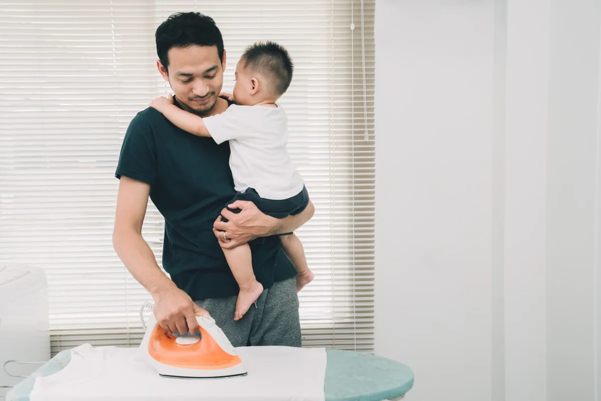 Father Ironing Clothes With a Baby in His Arms How Parenting Has Changed