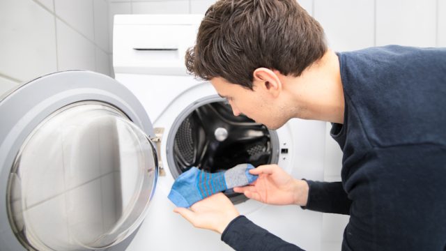 man holding one blue sock he pulled out of the laundry machine, the other one is missing