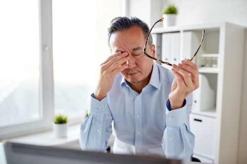 Mature asian man rubbing his eyes with tiredness