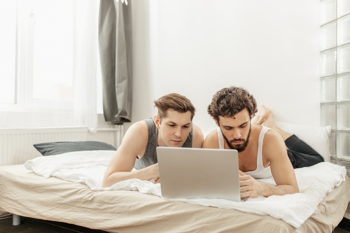 white male couple looking at a laptop in bed