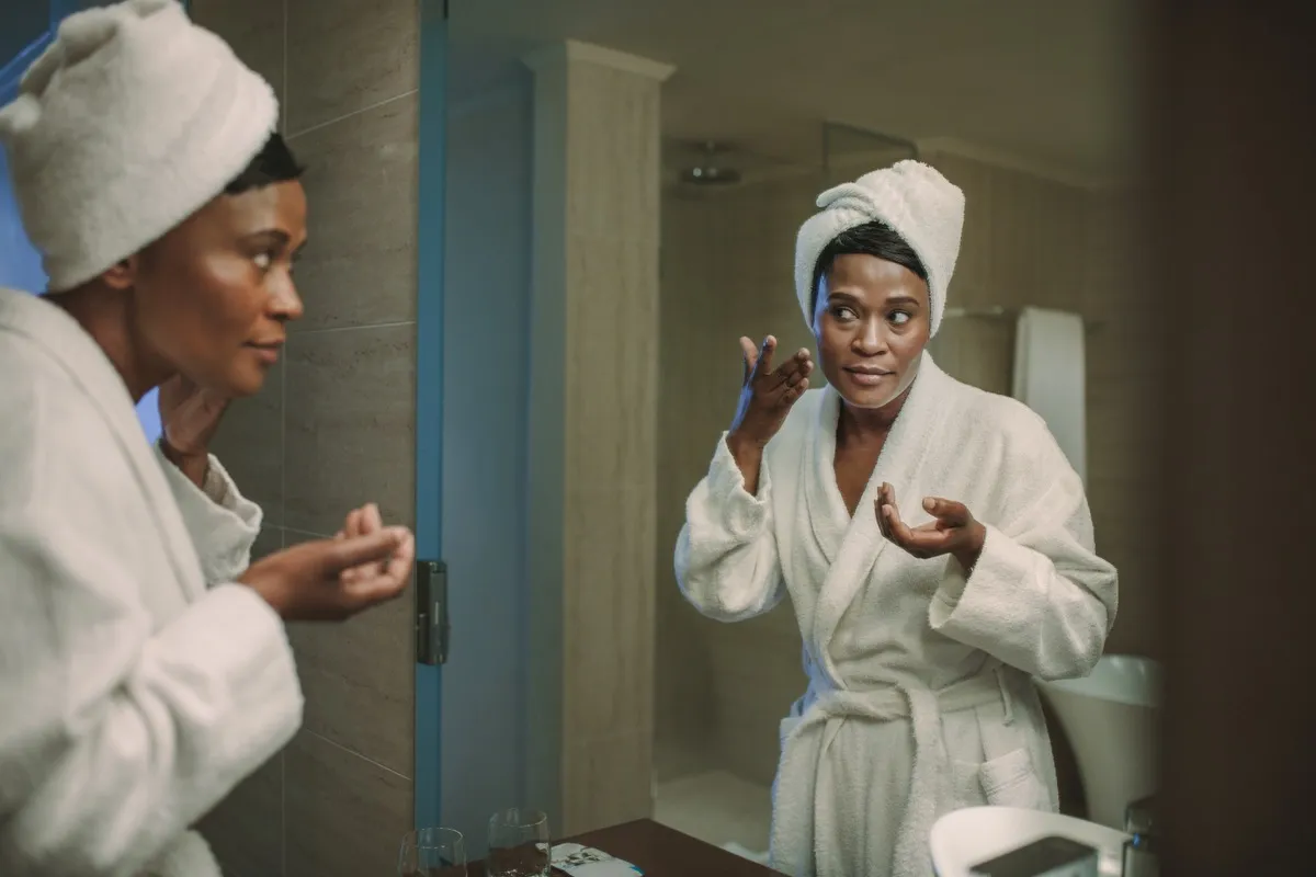 African American Woman Applying Face Cream in the Mirror Silent Health Symptoms