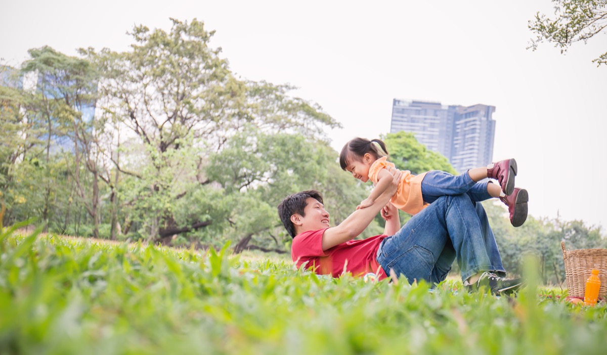 Asian Dad and Daughter play in grass in park, stay-at-home dad