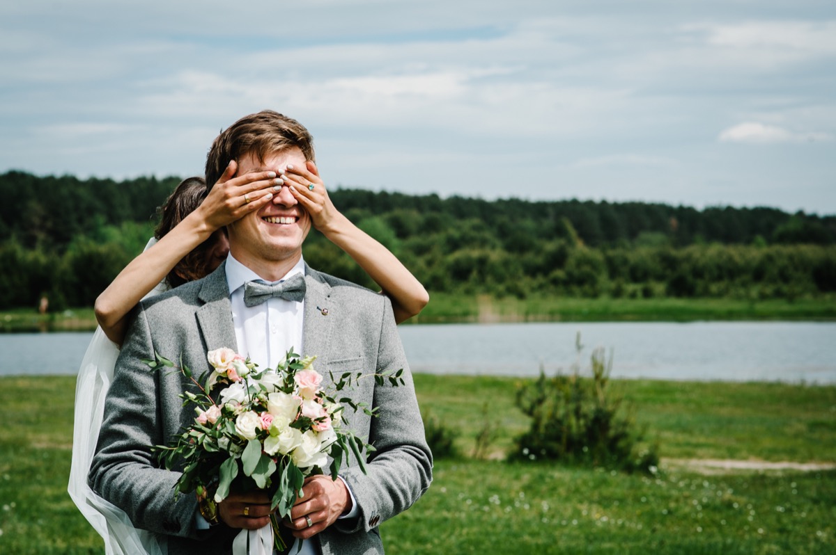woman covers man's eyes from behind during first look, craziest things brides and grooms have ever done at weddings