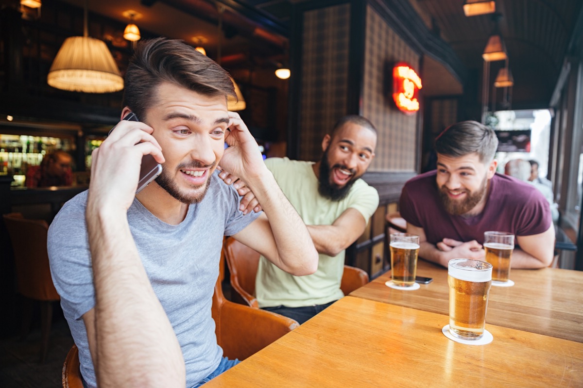 Man on phone in bar with friends drinking beer, things not to say to customer service