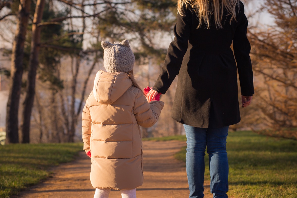 Mom and daughter hold hands walking through park in autumn, husband left while pregnant