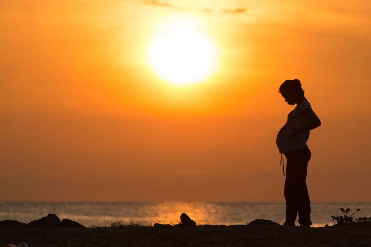 Pregnant teen stands on beach with sunset behind her, what it's like being a teen mom