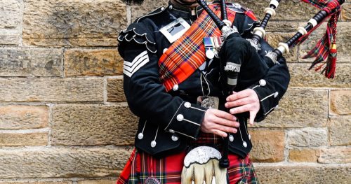 Scottish bagpiper standing against wall