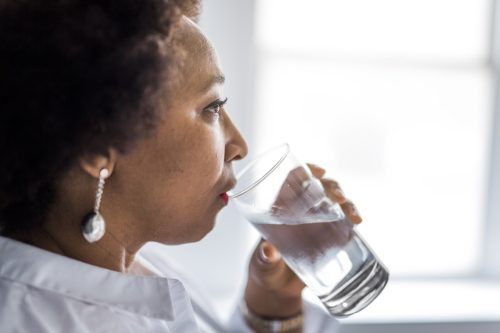 Black woman of middle age drinks water, ways you're damaging teeth