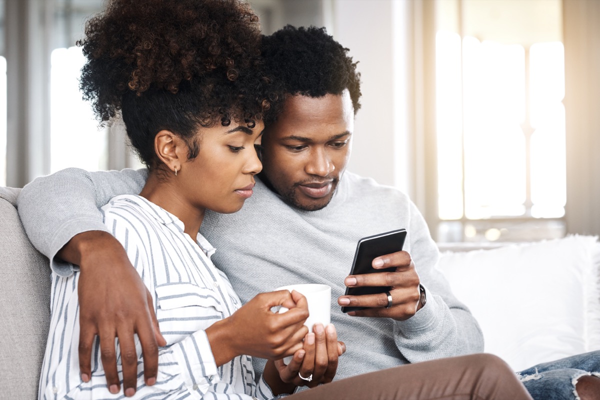 young black woman with coffee and young black man looking at a phone together
