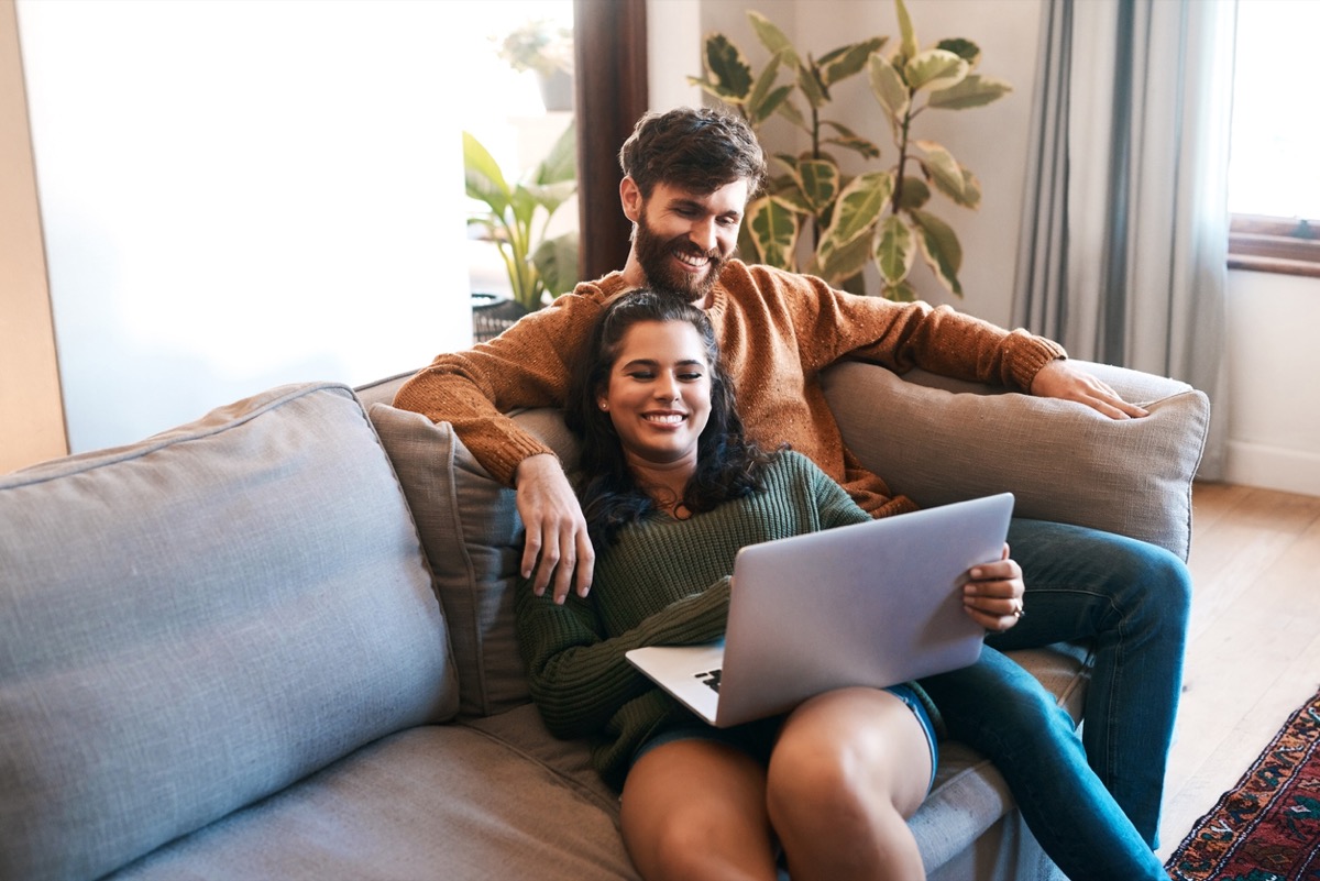 young white man and young white woman cuddling and smiling while on a laptop together