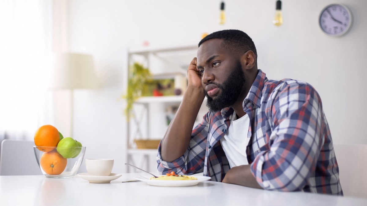 black man looking displeased with plate of food in front of him