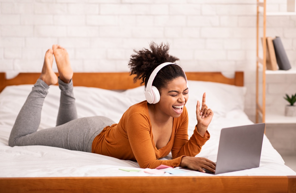 young black woman on bed singing on her computer with headphones