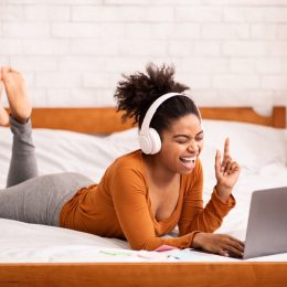 young black woman on bed singing on her computer with headphones