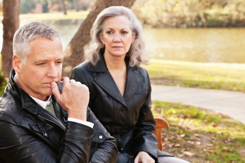 older white couple looking unhappy on a park bench
