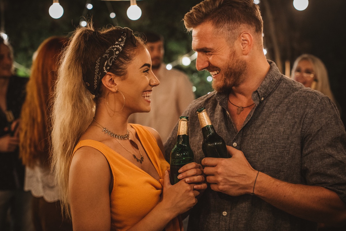 young white man and white woman holding beers and laughing at an outdoor party