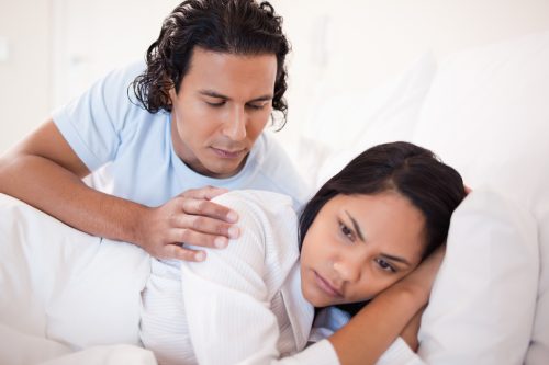 latino man comforting upset latino woman in bed