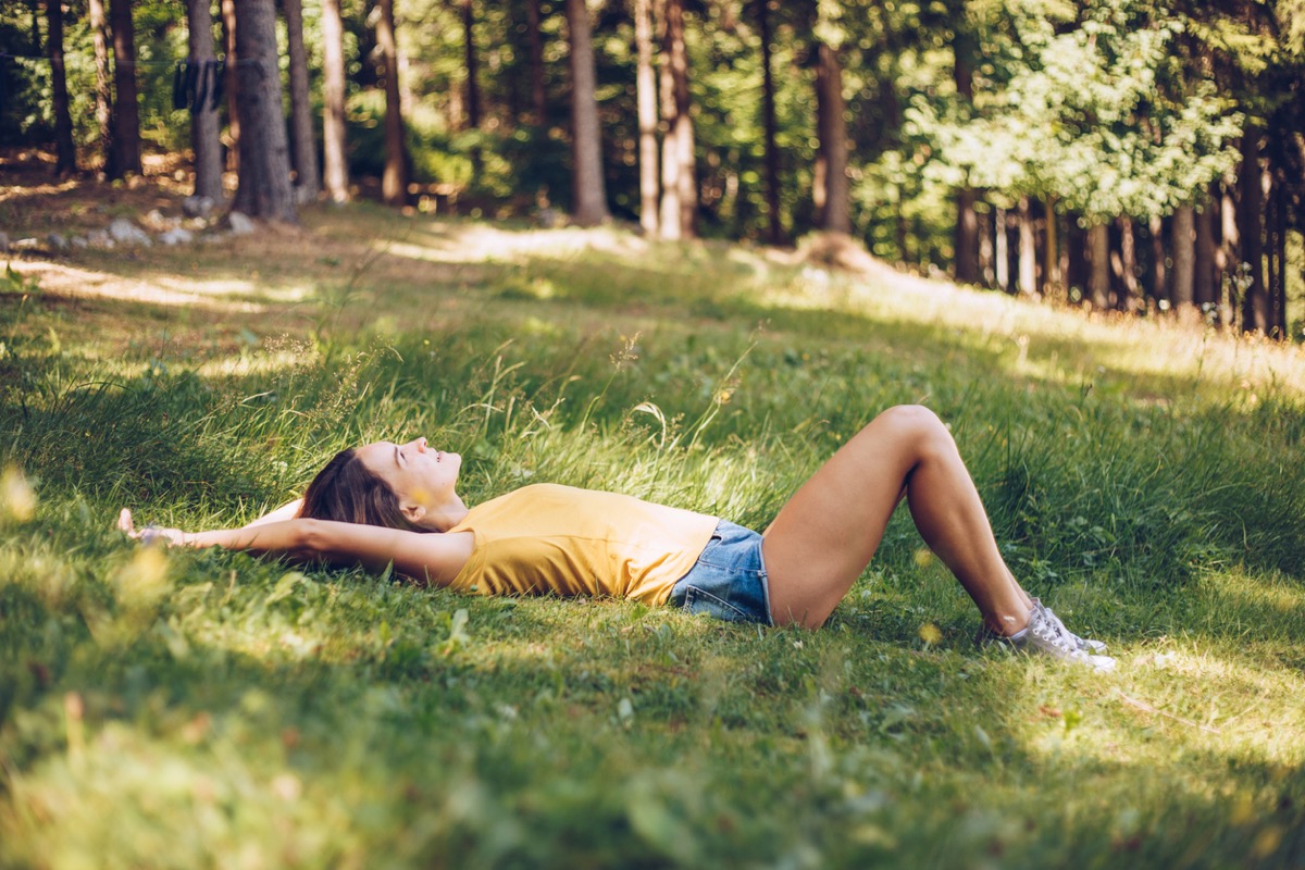 young white woman lying down on the grass by trees
