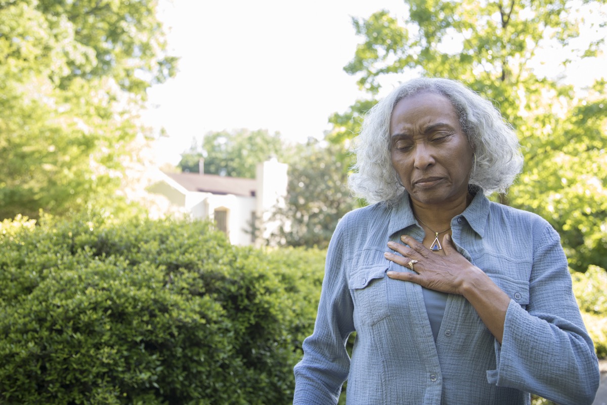 older black woman clutching her chest outside