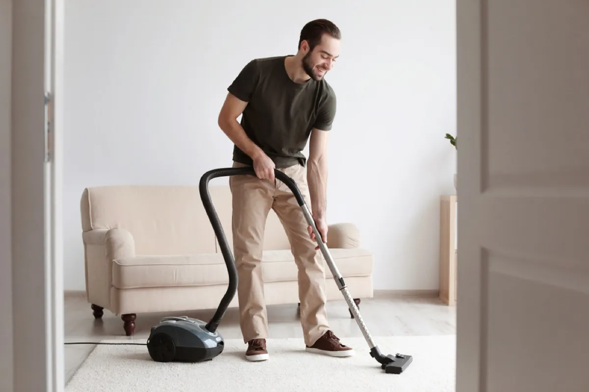 Shutterstock/New Africa. man vacuuming carpet and adjusting height of attac...