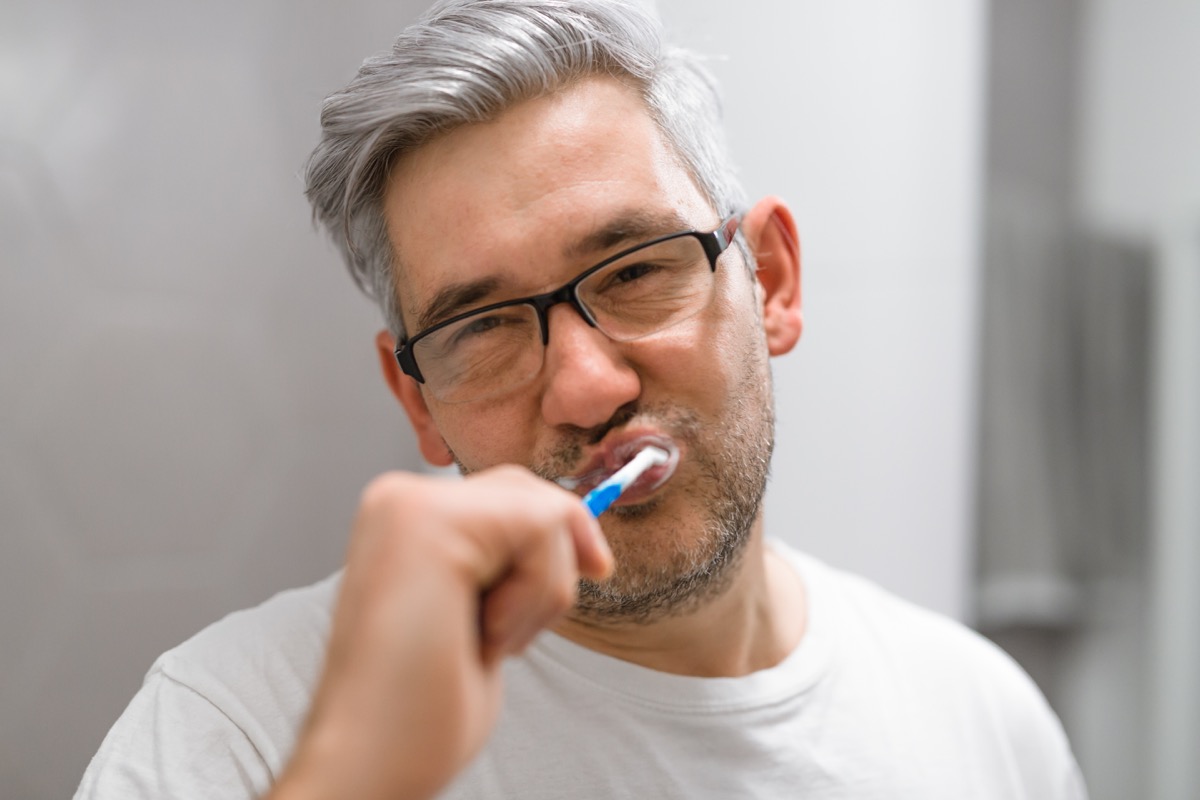 man with gray hair brushing teeth