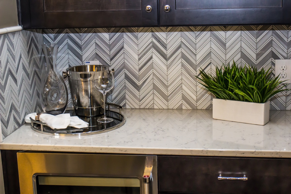 modern kitchen with dark cabinetry, white stone counters, and gray chevron backsplash
