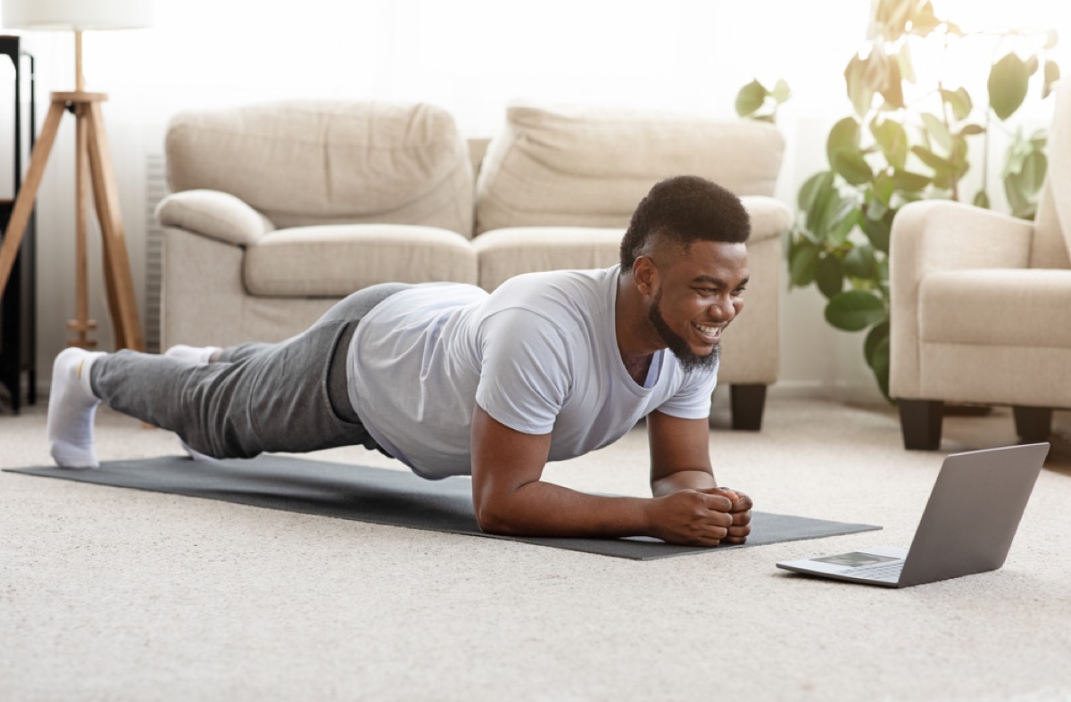 young black man doing a plank in front of his laptop at home