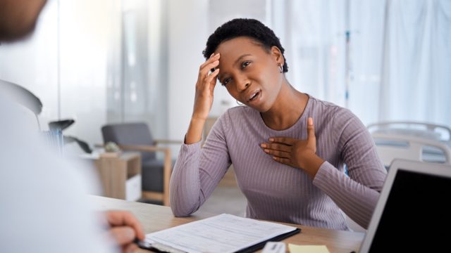 Black woman, doctor consultation and pain in chest, headache and explain for help, advice or medicine. African woman, patient and gesture to medic, nurse or healthcare expert for support in Atlanta