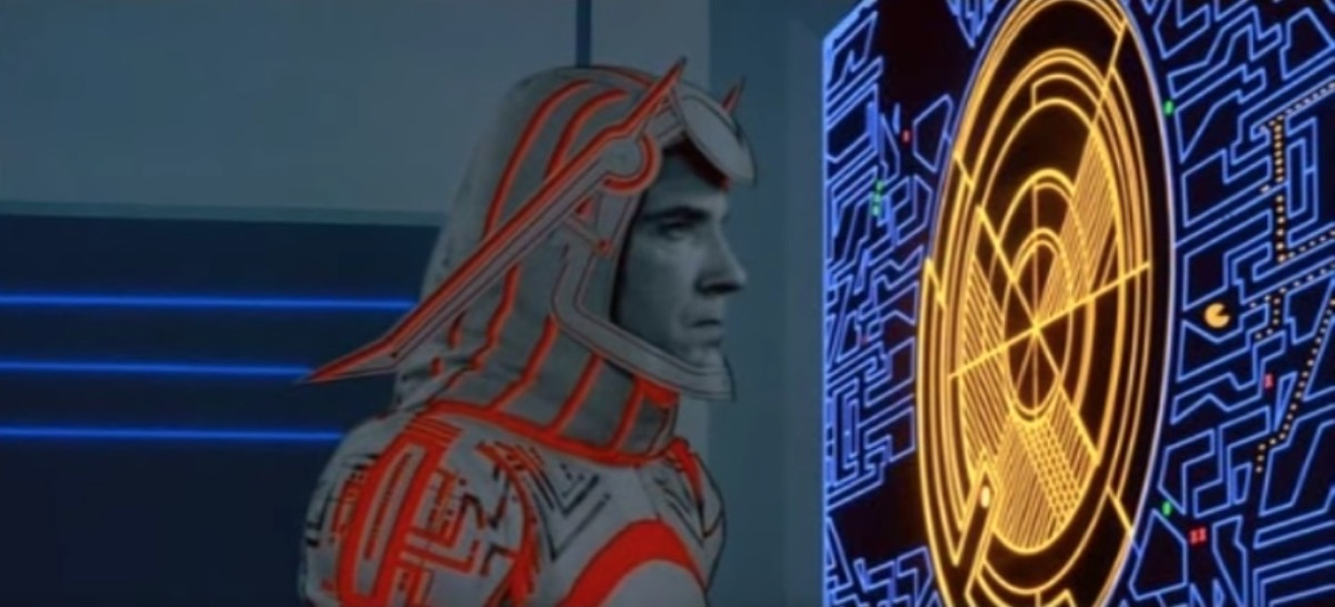 Tron movie character starring at a screen and in the corner, pac man is eating the white dots