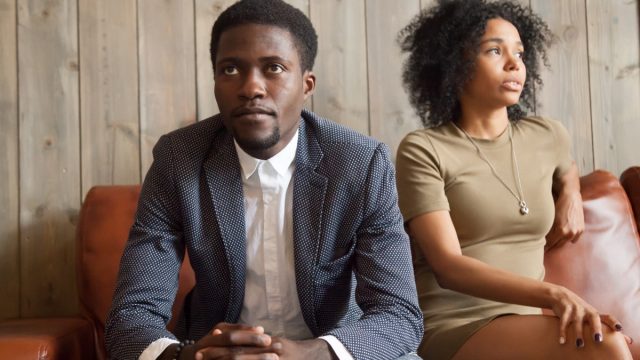 upset-looking 30-something black couple sitting on couch